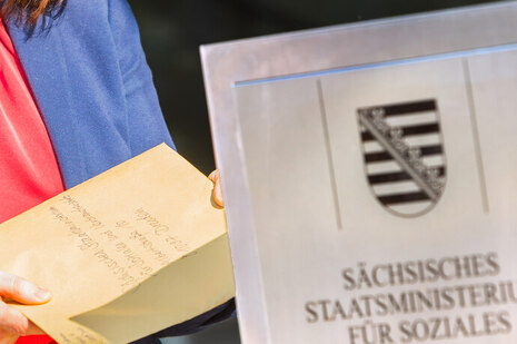Jemand schiebt einen Brief an das Sozialministerium in den Einwurfschlitz des SMS-Briefkastens