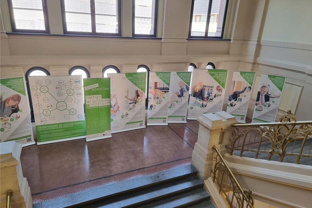 Roll-ups der Wanderausstellung der Sächsischen Opferbeauftragten 2023 im Treppenhaus der Polizeidirektion Dresden, einander gereiht vor hohen Fenstern, mit Texten und Bildern zu Hilfeangeboten für Betroffene.