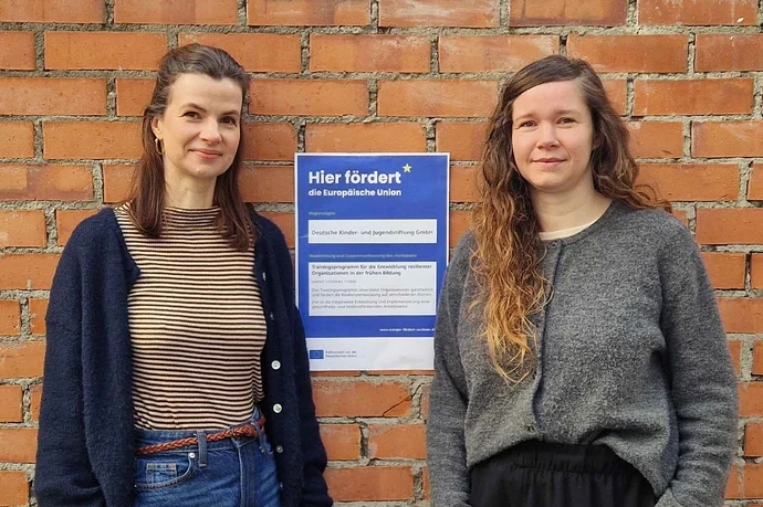 Zwei Frauen stehen vor einem Förderbescheid an einer Hauswand